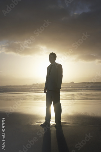 Silhouette of young businessman standing on beach at sunset