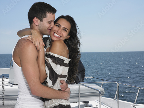 Young man kissing woman on yacht with ocean in background © moodboard