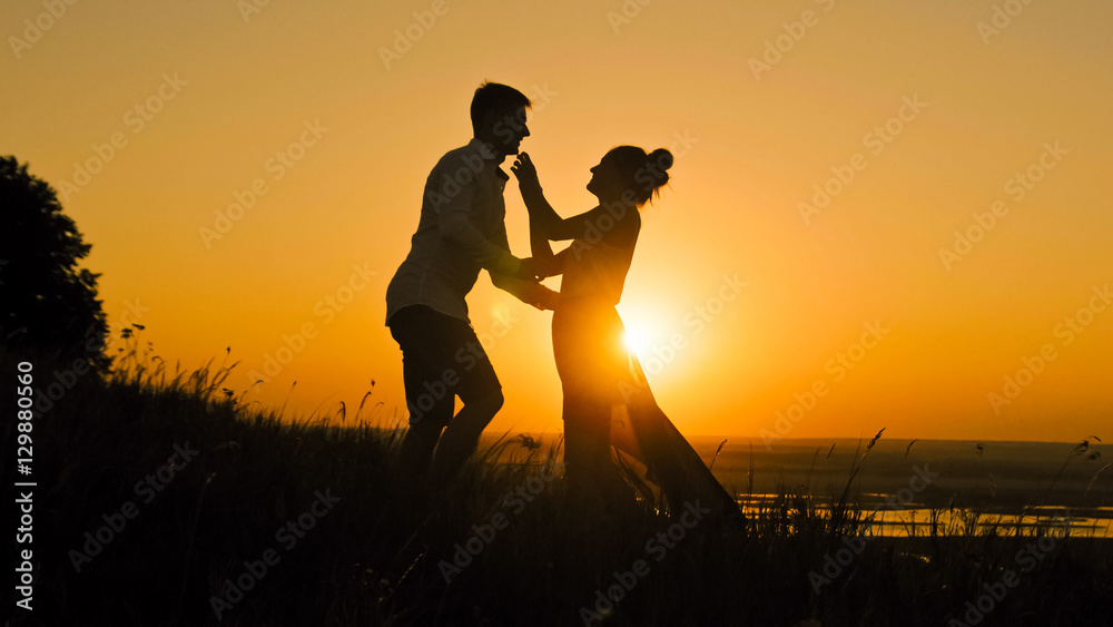 loving couple - brave young man and beautiful girl stands on high hill at sunset  have hugs  kiss, silhouette, slider shot