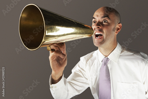 Tableau sur toile Bald businessman shouting through megaphone against gray background