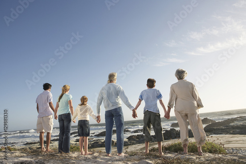 Rear view of three generation family holding hands on seashore photo