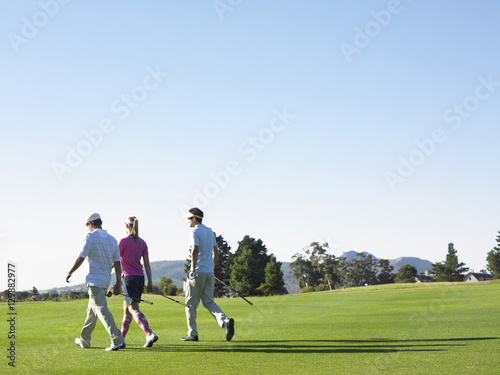 Rear view of three young golfers walking on golf course