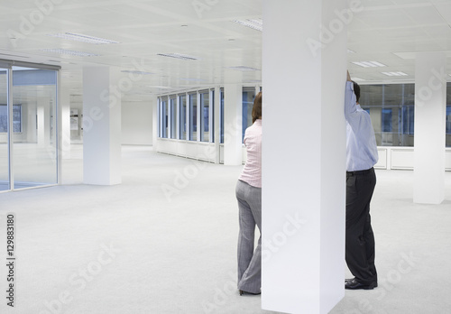 Rear view of businessman and businesswoman discussing behind column of empty office space