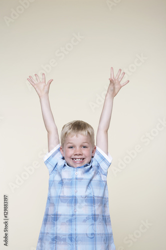 Portrait of an excited boy with hands raised on white background