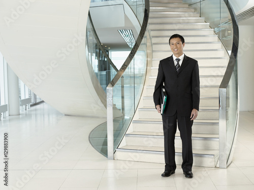 Full length portrait of a confident businessman with folder standing in front of stairs photo