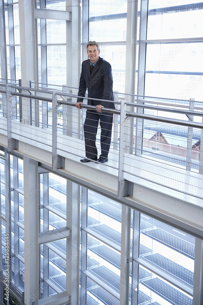 Full length portrait of happy middle aged businessman standing by railing in modern office Full length portrait of happy middle aged businessman standing by railing in modern office