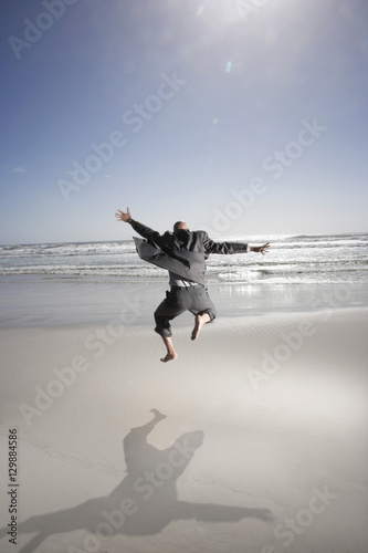 Rear view of middle aged businessman jumping on beach