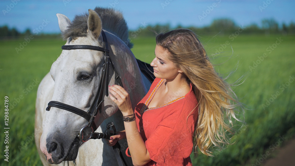 Obraz premium Beautiful blonde girl standing with a horse at a countryside