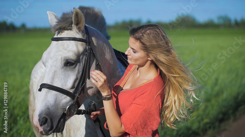 Beautiful blonde girl standing with a horse at a countryside