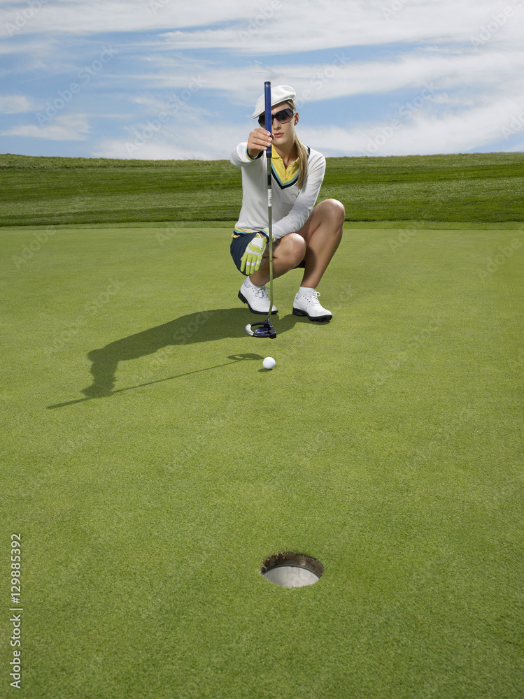 Full length of female golfer lining up a putt in golf course