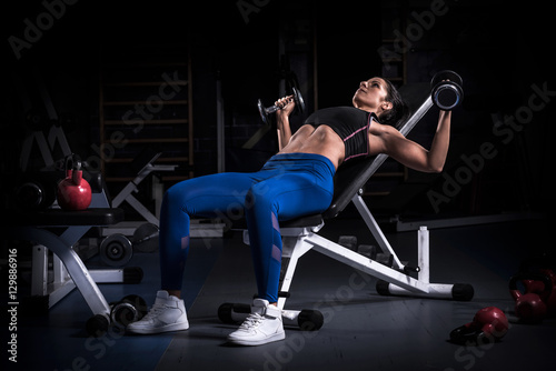 Woman bodybuilder in gym lifting dumbbells  on bench