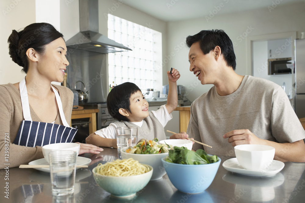 Happy young family enjoying meal at the kitchen table in house Happy young family enjoying meal at the kitchen table in house