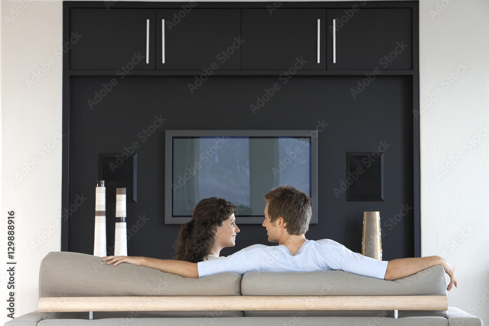 Romantic young couple looking at each other while relaxing on couch in living room Romantic young couple looking at each other while relaxing on couch in living room