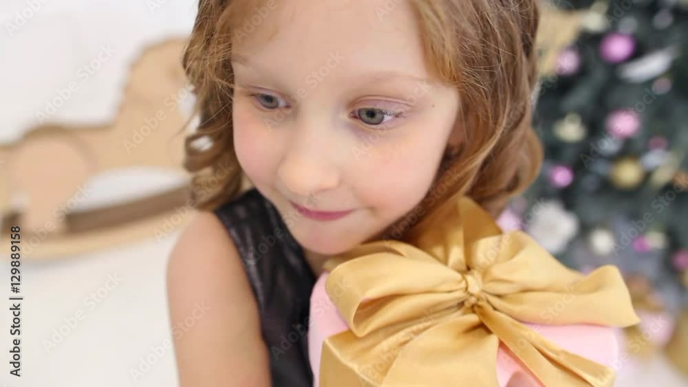 Close up portrait of cute happy face of little girl on Christmas morning in home interior. Child holding gift box happily. Christmas tree and presents in background. Real time full hd video footage. Close up portrait of cute happy face of little girl on Christmas morning in home interior. Child holding gift box happily. Christmas tree and presents in background. Real time full hd video footage.