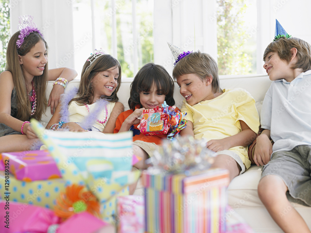 Obraz premium Children sitting on sofa at birthday party as one open the gift