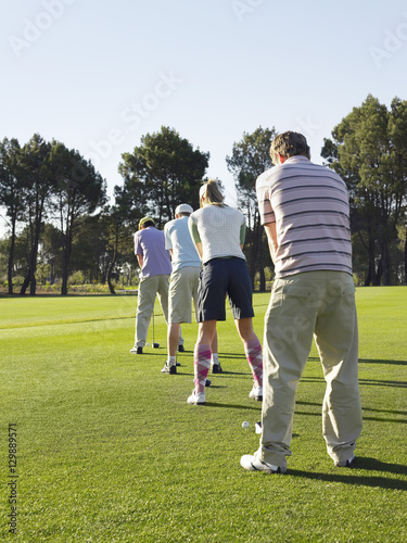 Rear view of young golfers standing in row teeing off on golf course photo