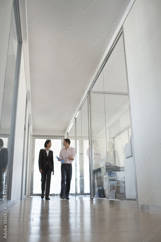 Two business people walking while talking in hallway Two business people walking while talking in hallway