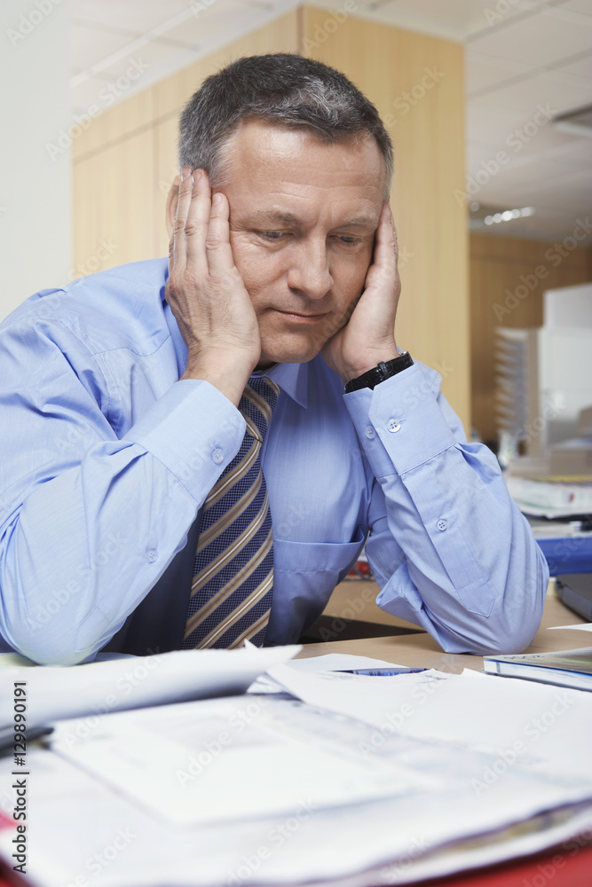 Pensive middle aged businessman sitting at office desk Pensive middle aged businessman sitting at office desk