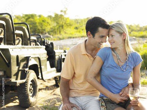 Loving young couple with wineglass with jeep in the background