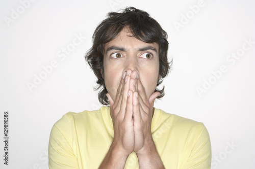 Handsome man covering mouth with both hands on white background