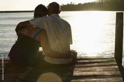 Rear view of happy senior couple sitting on edge of pier by lake