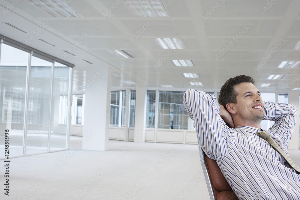 Smiling young businessman relaxing on chair in empty office space Smiling young businessman relaxing on chair in empty office space