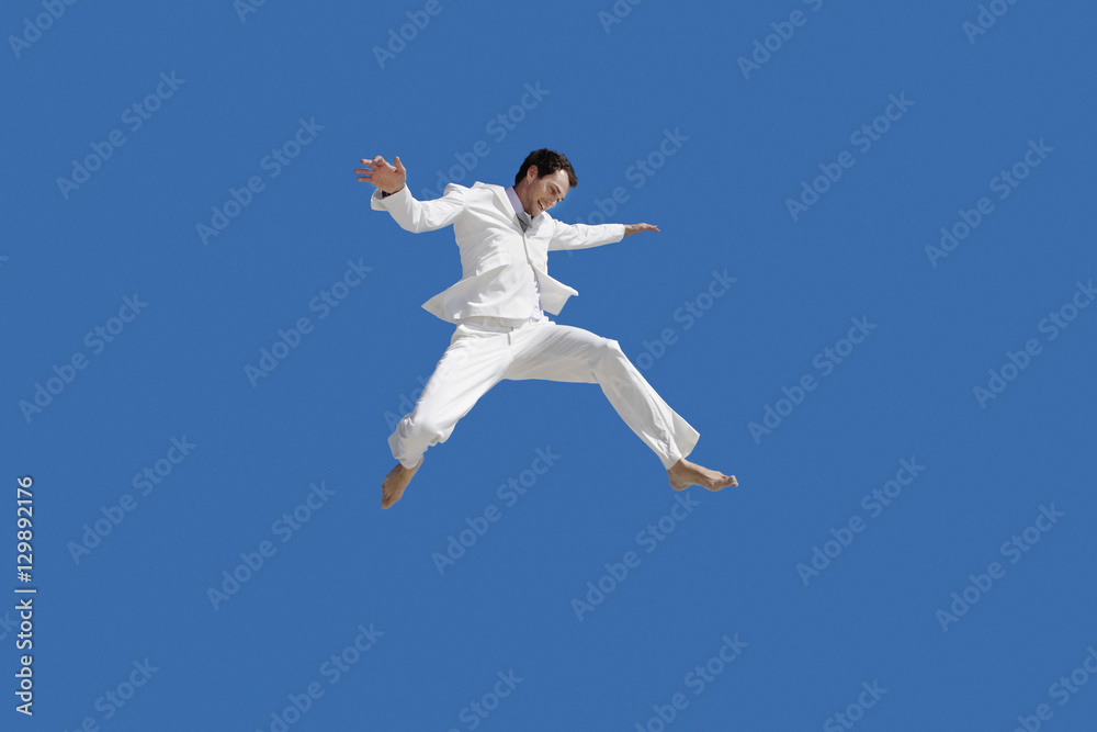 Full length of young businessman jumping against blue sky Full length of young businessman jumping against blue sky