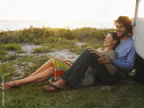 Slika na platnu Full length of young couple on beach leaning on campervan