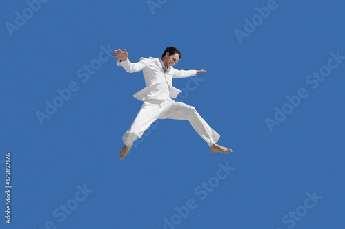 Full length of young businessman jumping against blue sky