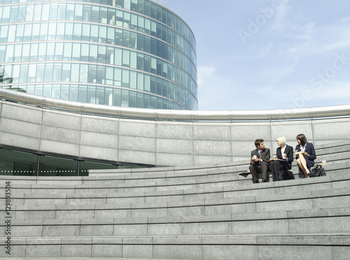 Photography Full length of three business people sitting on steps outside office building du