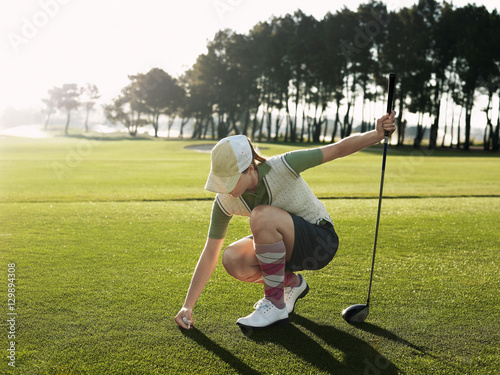 Full length of young female golfer placing ball on tee