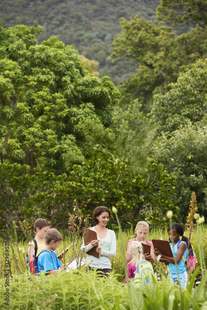 Obraz premium Young teacher with children preparing notes on clipboards during field trip