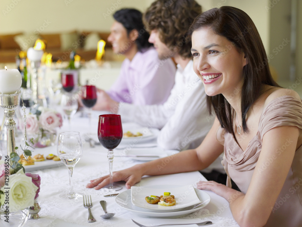 Cheerful young woman sitting with friends at dinner party Cheerful young woman sitting with friends at dinner party
