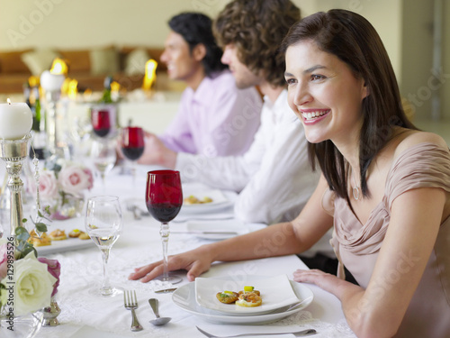 Cheerful young woman sitting with friends at dinner party