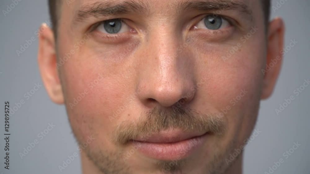 Close up young man's face lightly smiling, gray background Close up young man's face lightly smiling, gray background