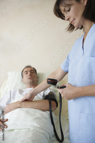 Cropped nurse taking blood pressure and pulse of patient in hospital bed © moodboard