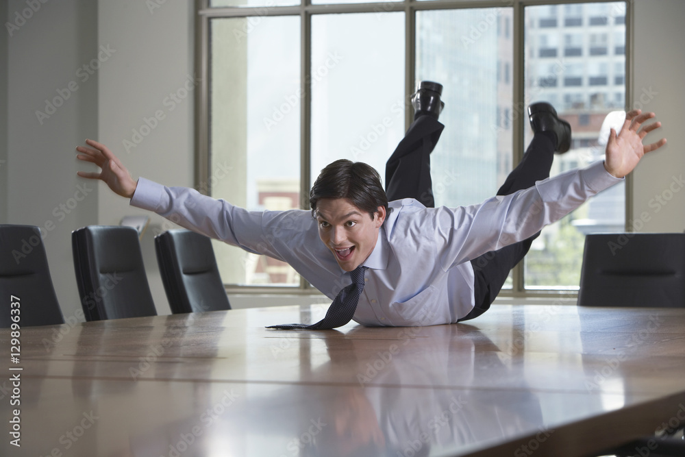 Young businessman sliding on stomach on conference table - obrazy, fototapety, plakaty 