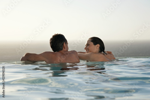 Rear view of happy couple relaxing in infinity pool at resort