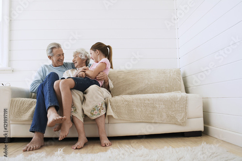 Full length of happy senior couple sitting with granddaughter on couch