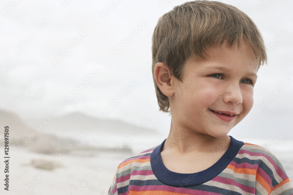 Closeup of cute little boy smiling while looking away at beach Closeup of cute little boy smiling while looking away at beach