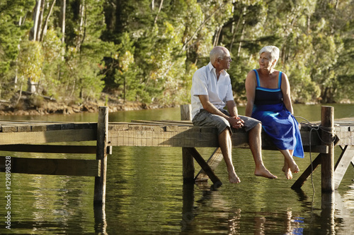 Full length of happy senior couple sitting on pier at lake photo