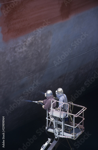 Two People standing in crane bucket Painting Large Ship