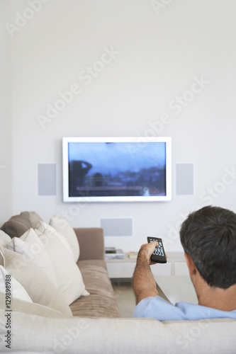 Rear view of middle aged man watching television in living room