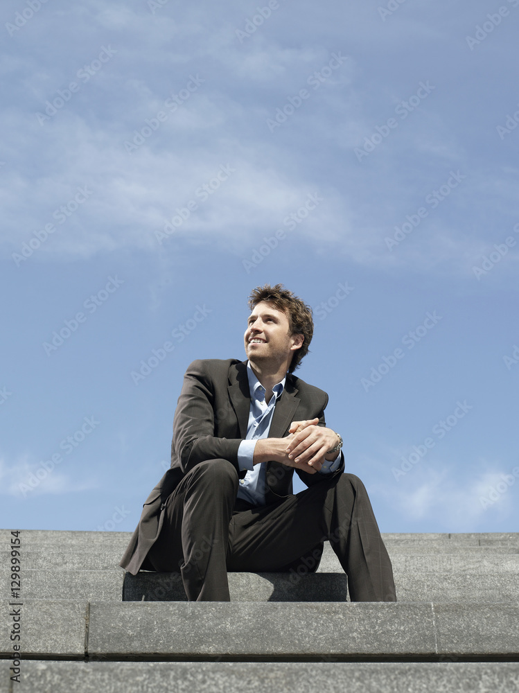 Low angle view of happy young businessman sitting on steps against sky