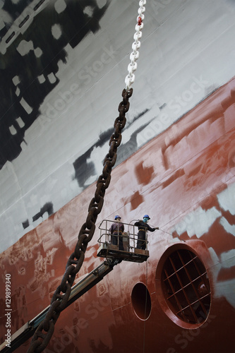 Two men in cherry picker working at ship in dry dock low angle view