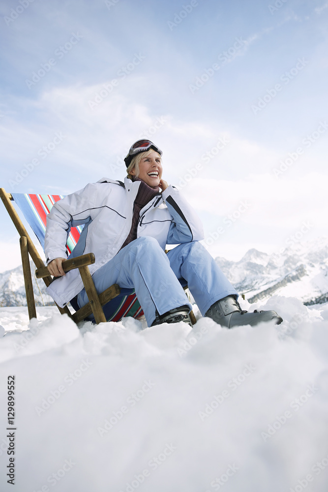Low angle view of a smiling woman sitting on deckchair in snowy mountains Low angle view of a smiling woman sitting on deckchair in snowy mountains