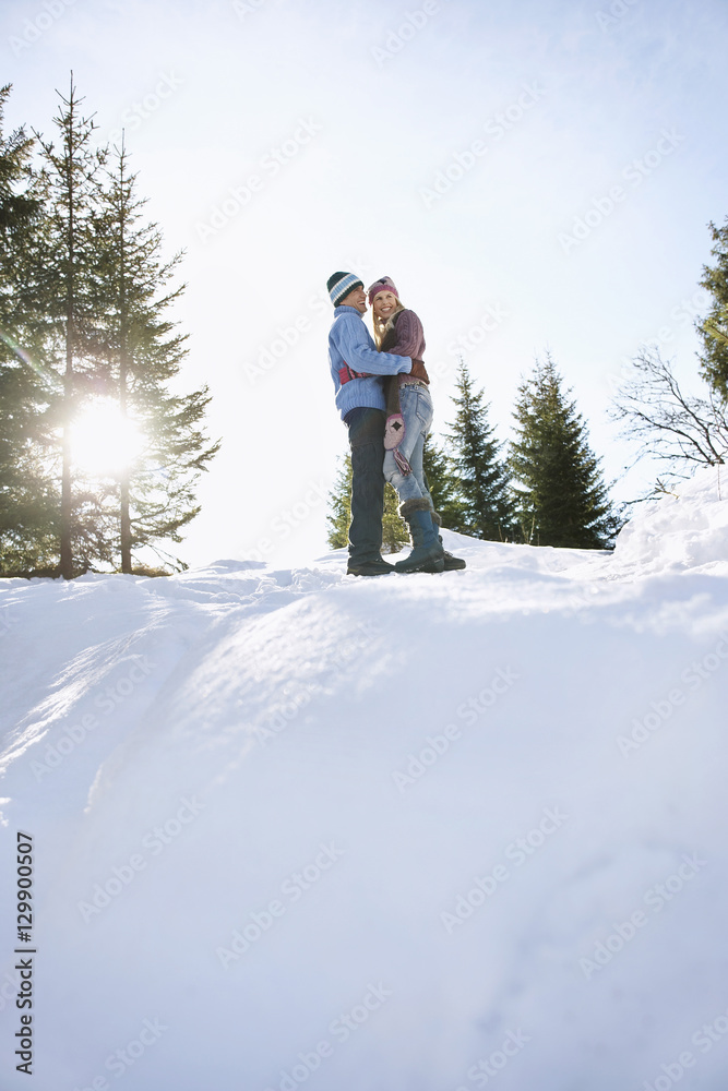 Full length low angle view of a loving couple standing on snow covered hill