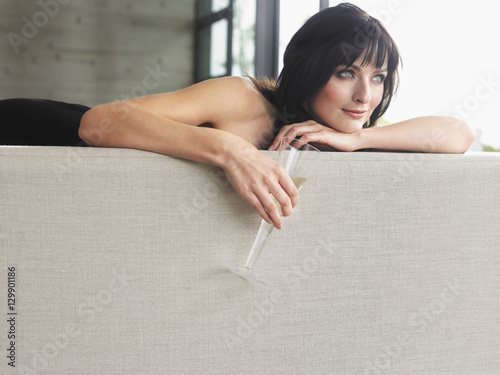 Beautiful young woman with champagne glass leaning on couch