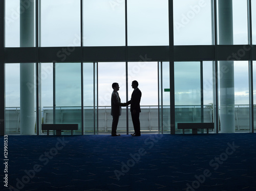 Side view of two silhouette businessmen shaking hands in the airport lobby