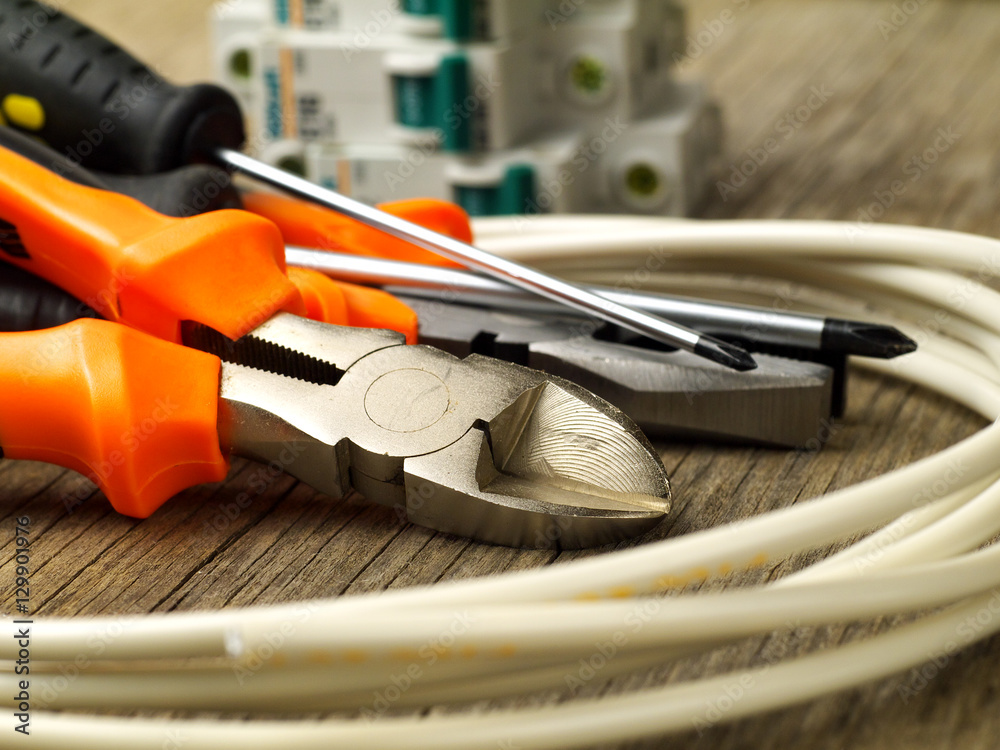 set of electrician tools, a coil of wire and switches in background, focus on cutter set of electrician tools, a coil of wire and switches in background, focus on cutter